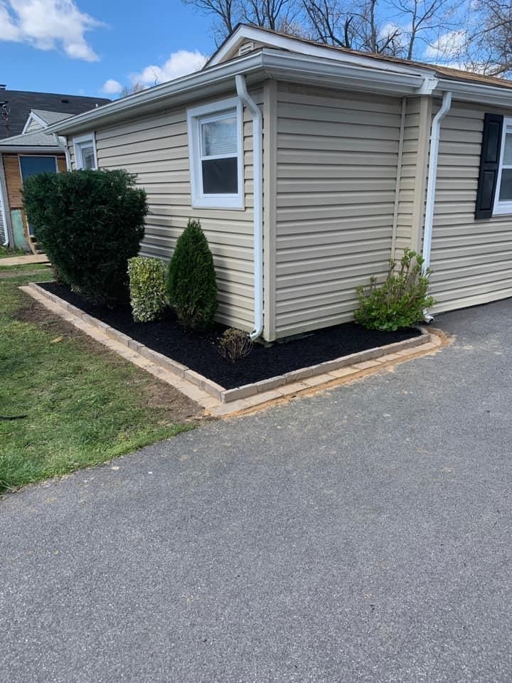 A small house with a garden and mulch in front of it and a driveway.