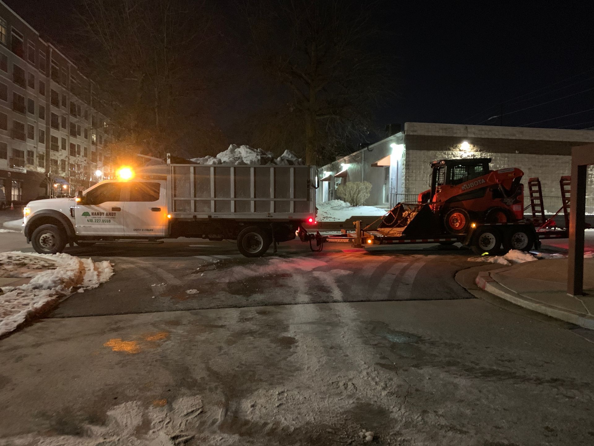 A truck is towing a tractor in the snow at night.