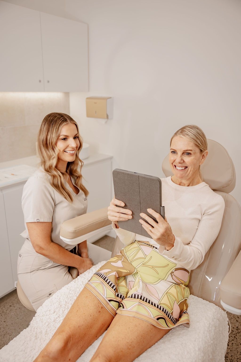 A Woman is Sitting in a Chair Looking at a Tablet — Gorjess Aesthetics in Corrimal, NSW