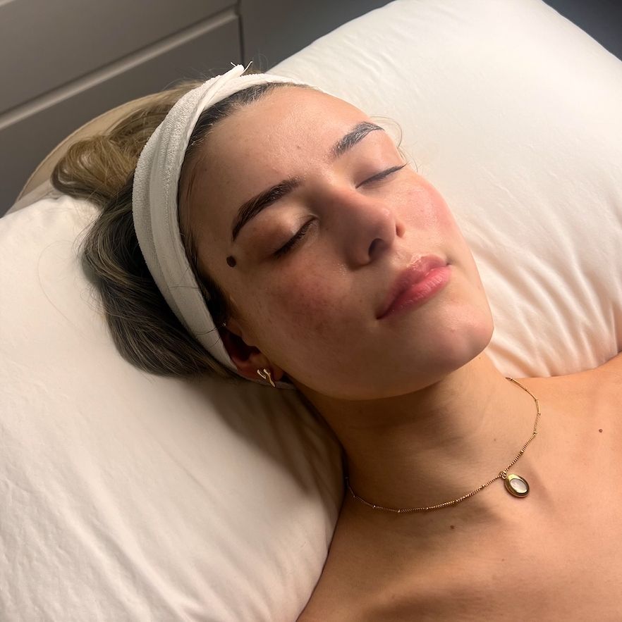 A Woman is Laying on a Bed With Her Eyes Closed — Gorjess Aesthetics in Corrimal, NSW