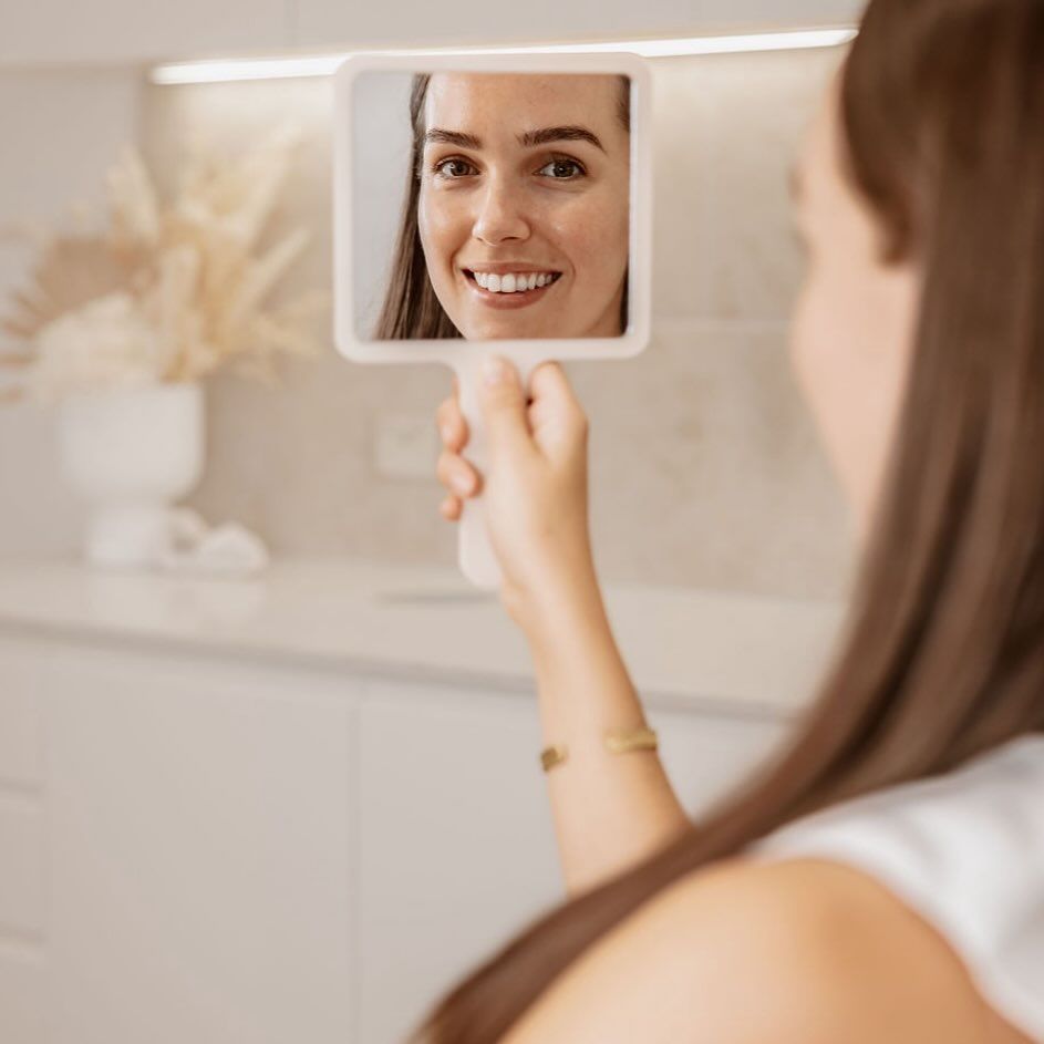 A Woman is Looking at Her Reflection in a Hand Mirror — Gorjess Aesthetics in Corrimal, NSW