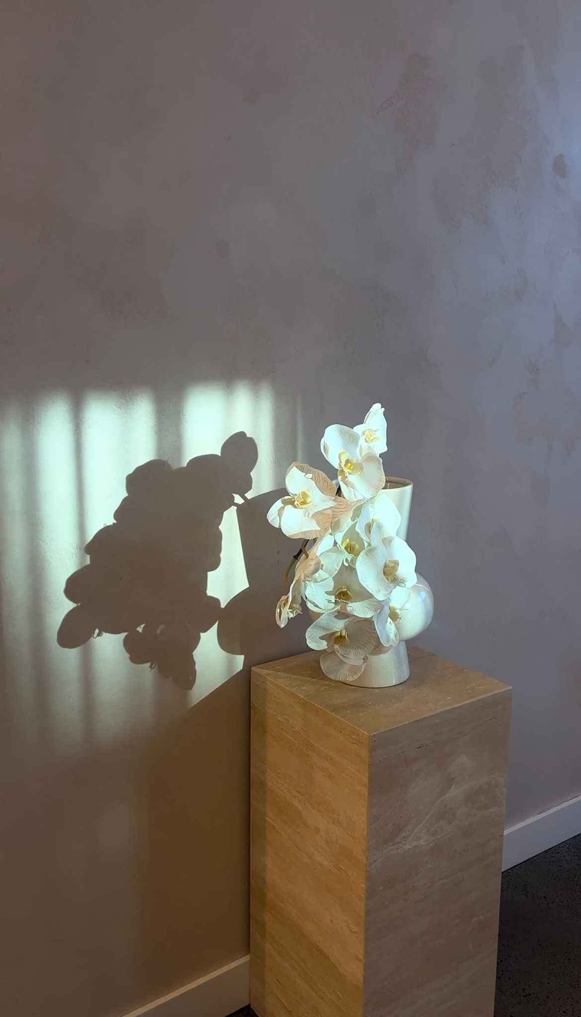 A Vase of Flowers is Sitting on a Wooden Pedestal in Front of a Window — Gorjess Aesthetics in Corrimal, NSW