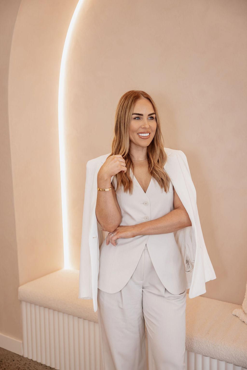 A Woman in a White Suit is Standing in a Room With Her Arms Crossed — Gorjess Aesthetics in Corrimal, NSW
