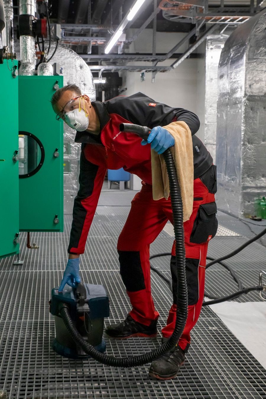 Ein Mann mit Maske und Handschuhen reinigt eine Maschine mit einem Staubsauger.