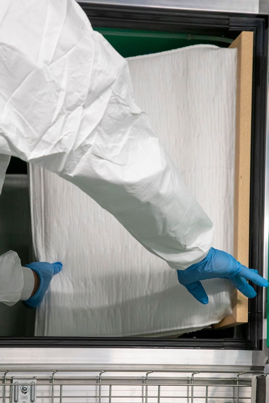 Eine Person in einem Schutzanzug und blauen Handschuhen öffnet eine Tür.