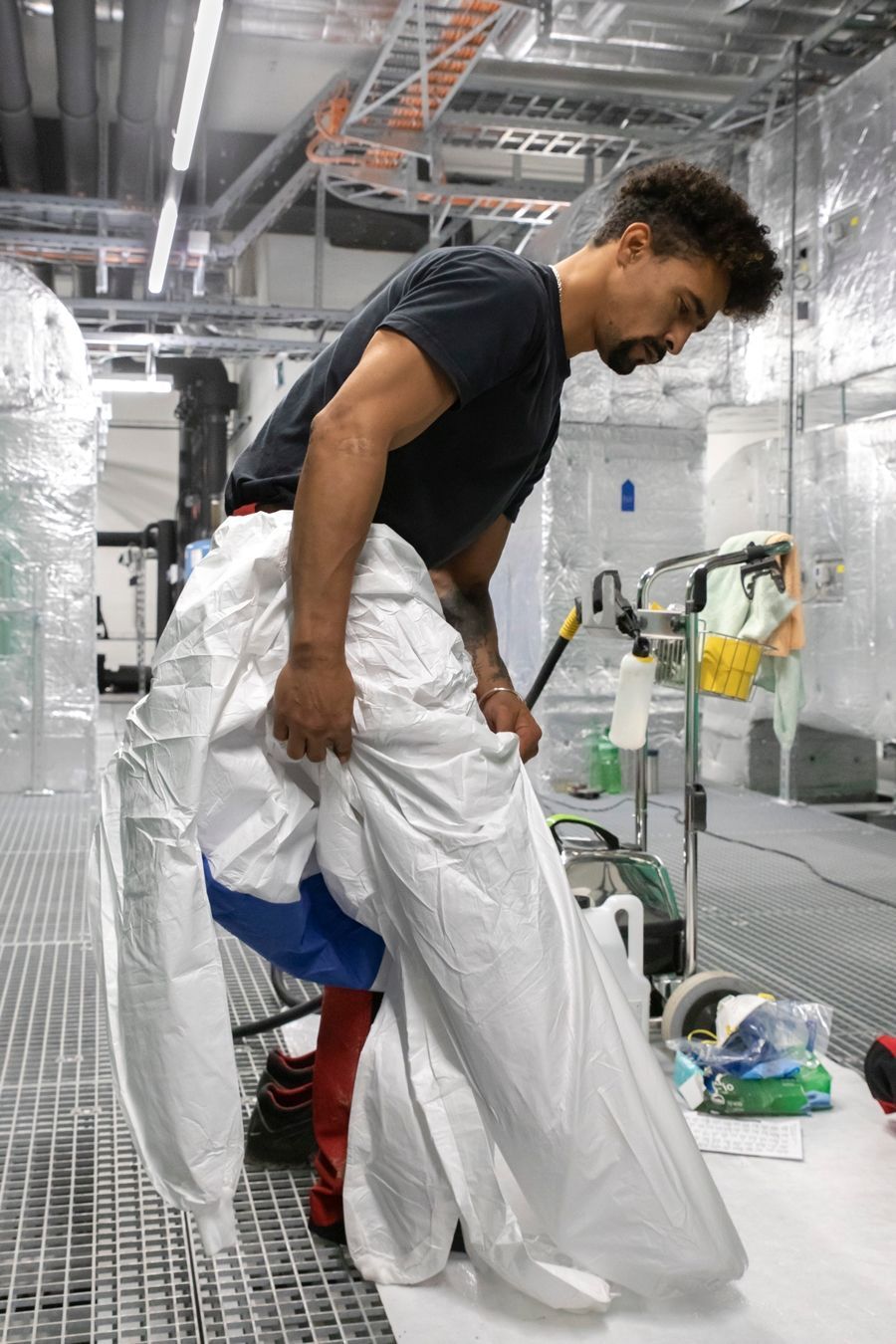 Ein Mann in einem schwarzen Hemd und weissen Hosen steht in einem Raum.