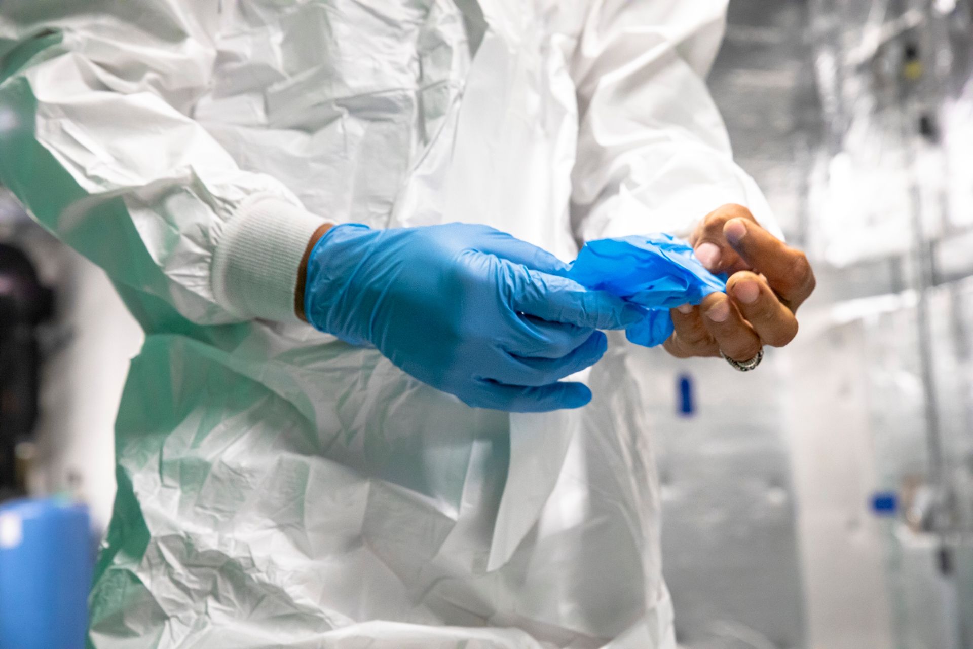 Eine Person mit Schutzanzug und blauen Handschuhen hält einen blauen Gegenstand.