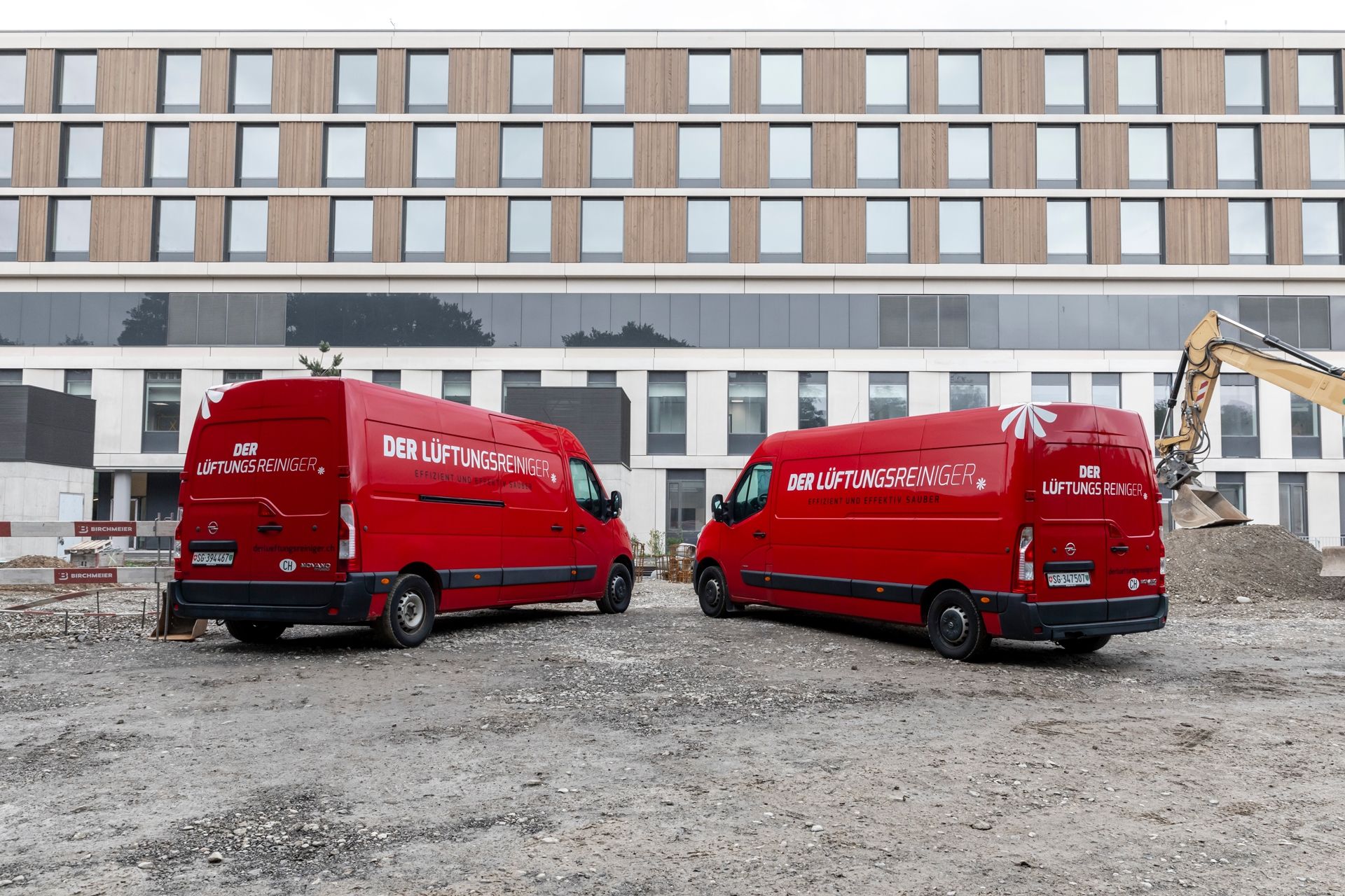 Zwei rote Lieferwagen parken vor einem grossen Gebäude.