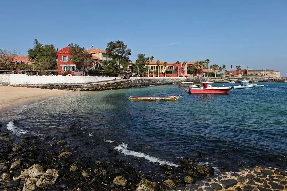 A beach with boats in the water and buildings in the background.