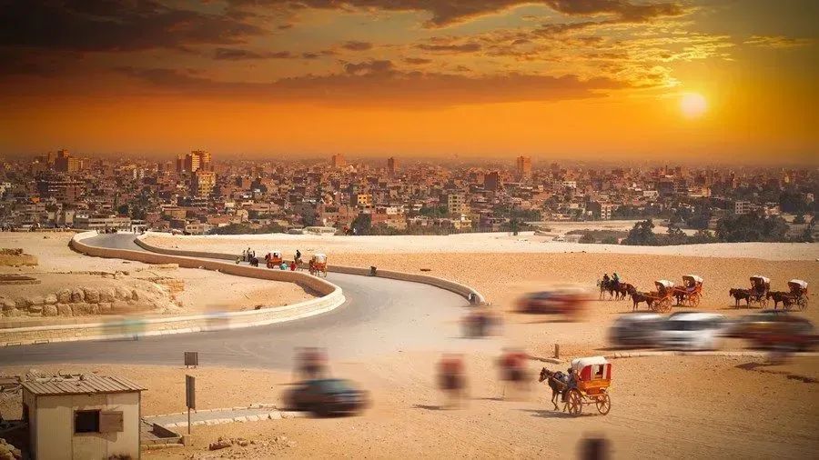 A horse drawn carriage is driving down a desert road.