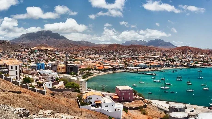 An aerial view of a city with boats in the water and mountains in the background.