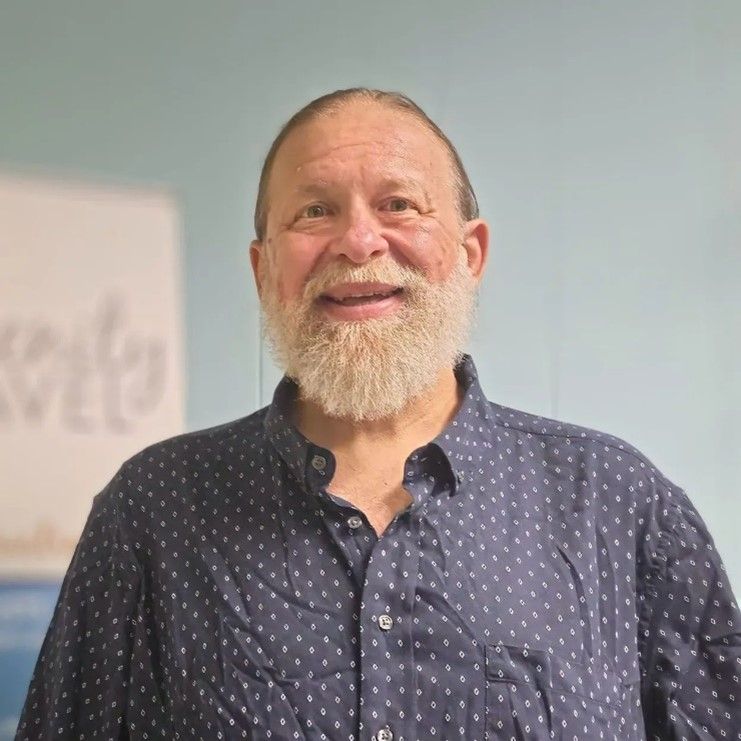 A woman wearing glasses and a pink shirt is smiling.