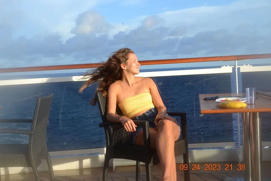 A woman is sitting in a chair on a balcony overlooking the ocean.