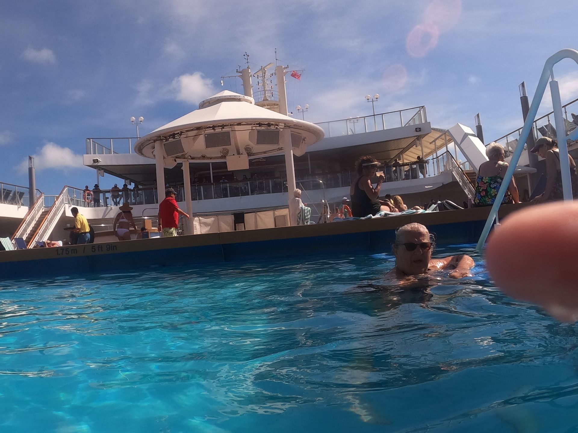 Person swimming in a pool with a cruise ship in the background on a sunny day.
