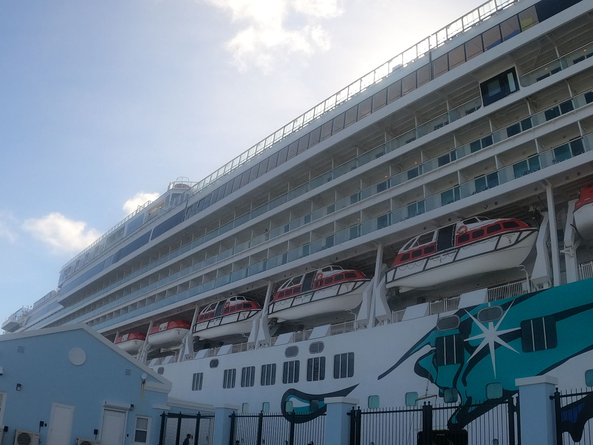 Large cruise ship docked at a pier, white with blue and red accents.