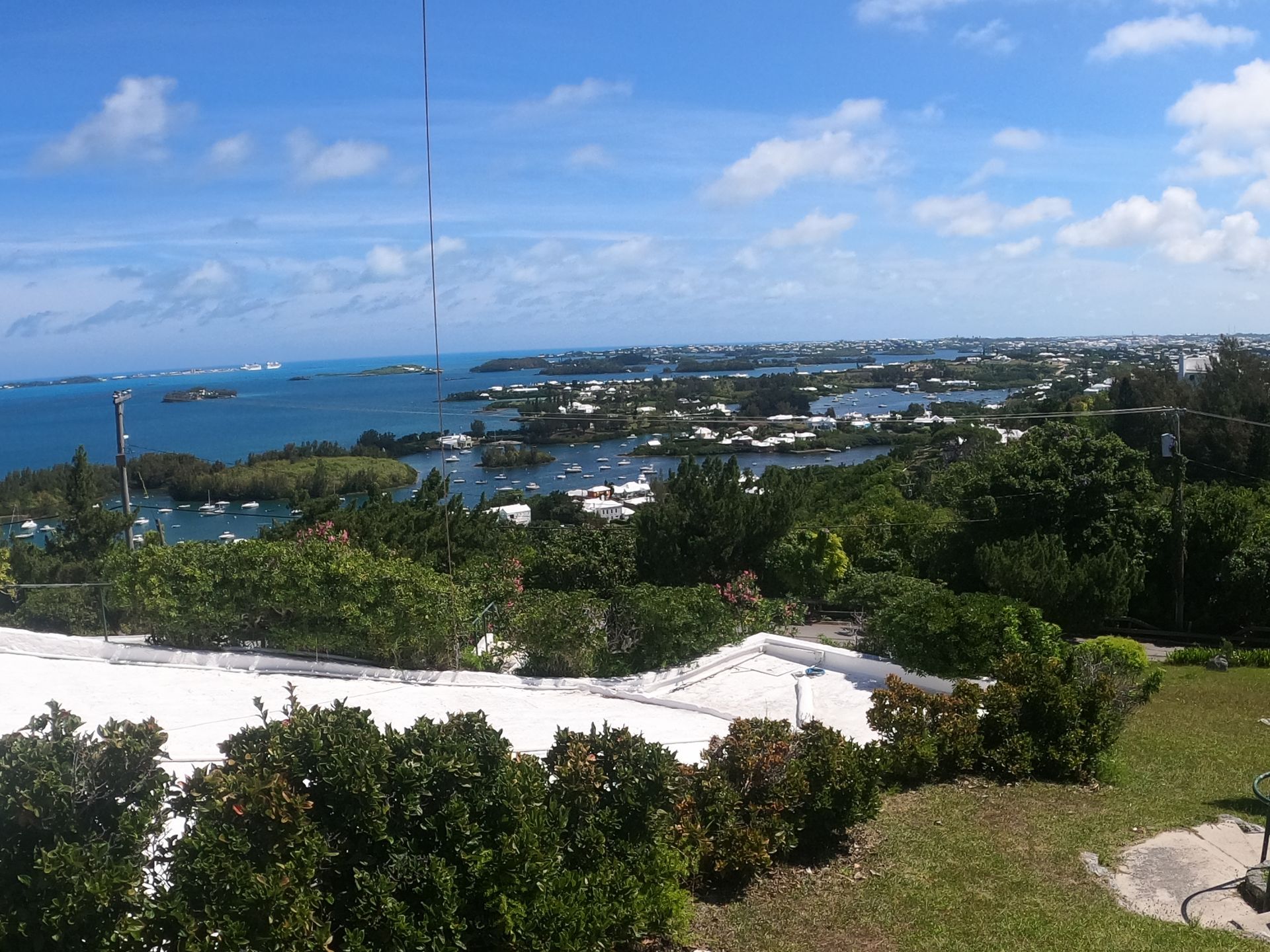 Scenic view of Bermuda: turquoise water, green trees, white buildings, and blue sky with clouds.