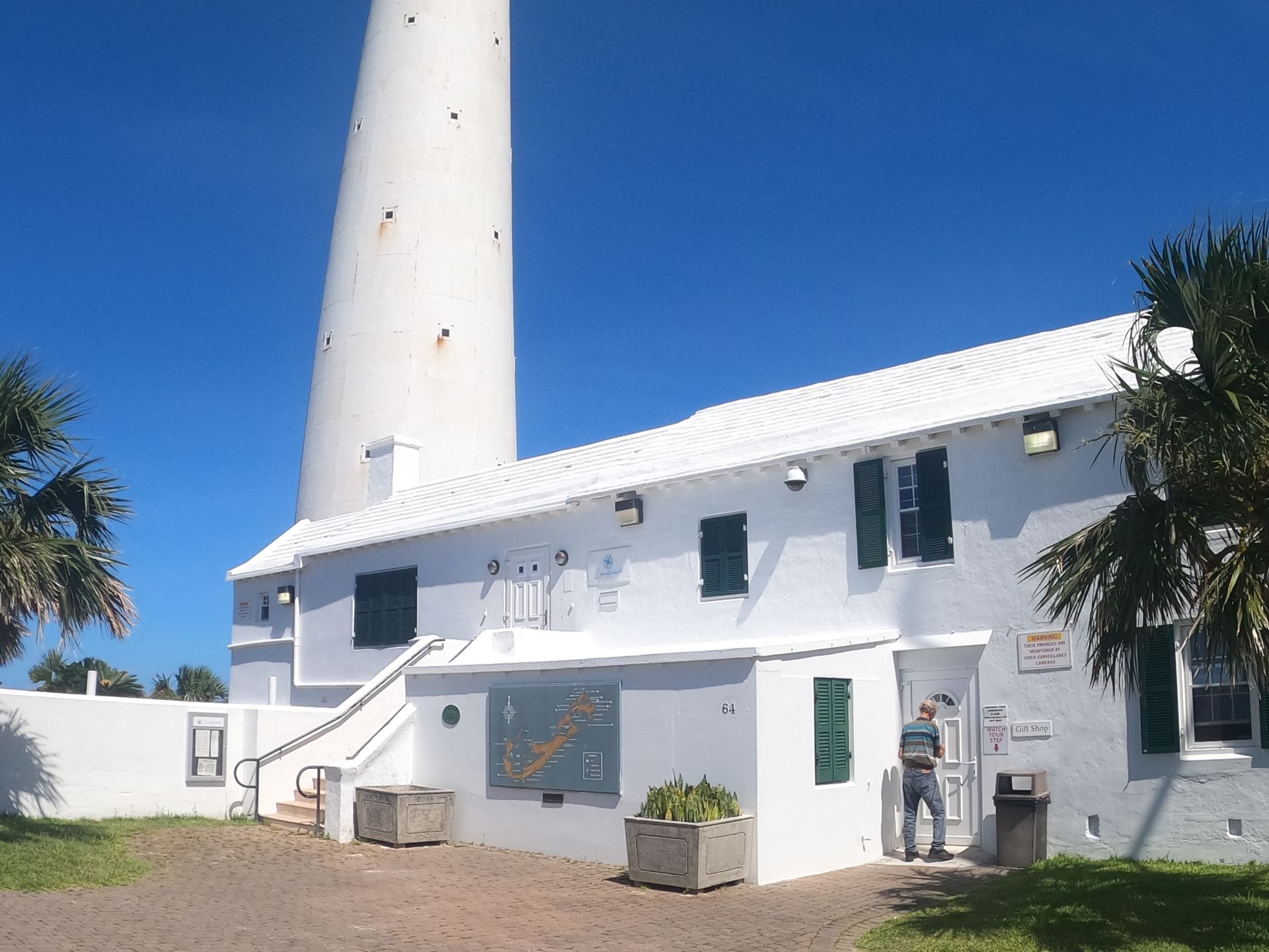 A white lighthouse with a connecting building, clear blue sky, and a person standing near the entrance.
