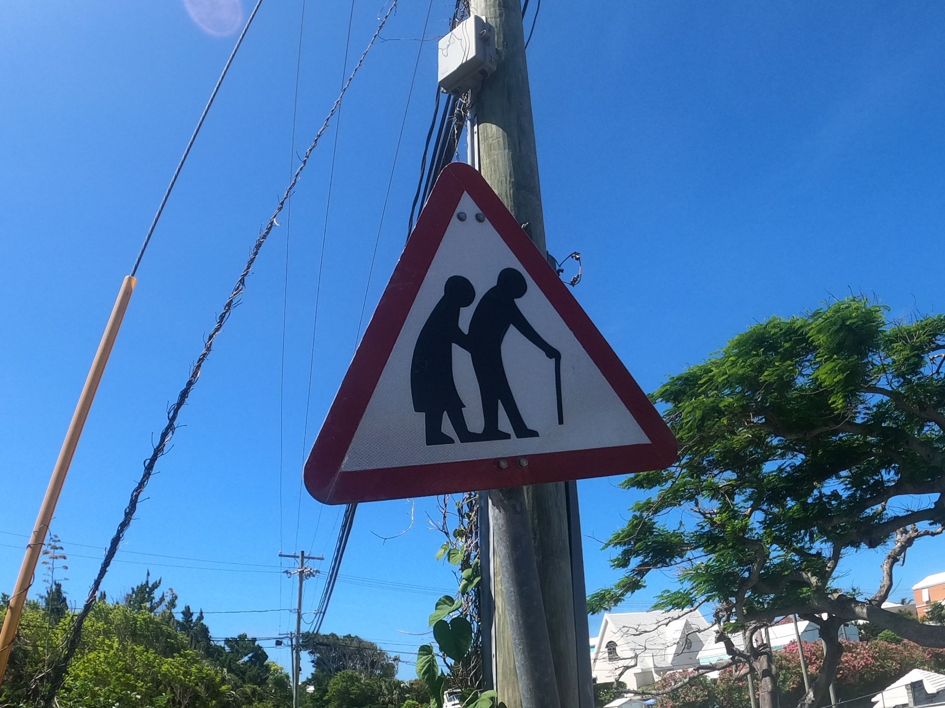 Warning sign: Elderly people crossing. Red triangle, white background, blue sky.