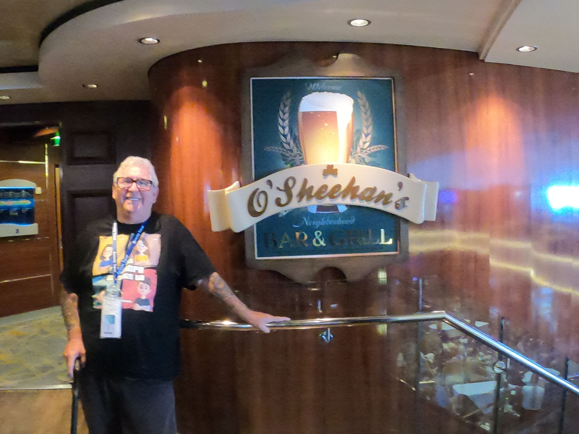 Man standing at O'Sheehan's Bar & Grill sign on a cruise ship. He's wearing a black shirt and holding a cane.