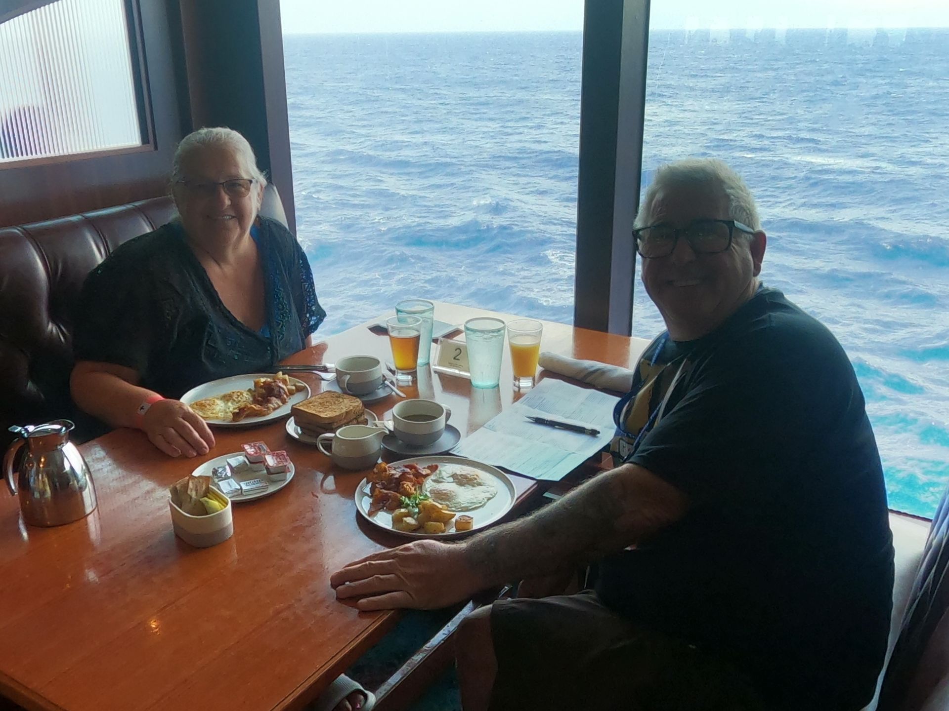 Two people eating breakfast at a table by a window overlooking the ocean.