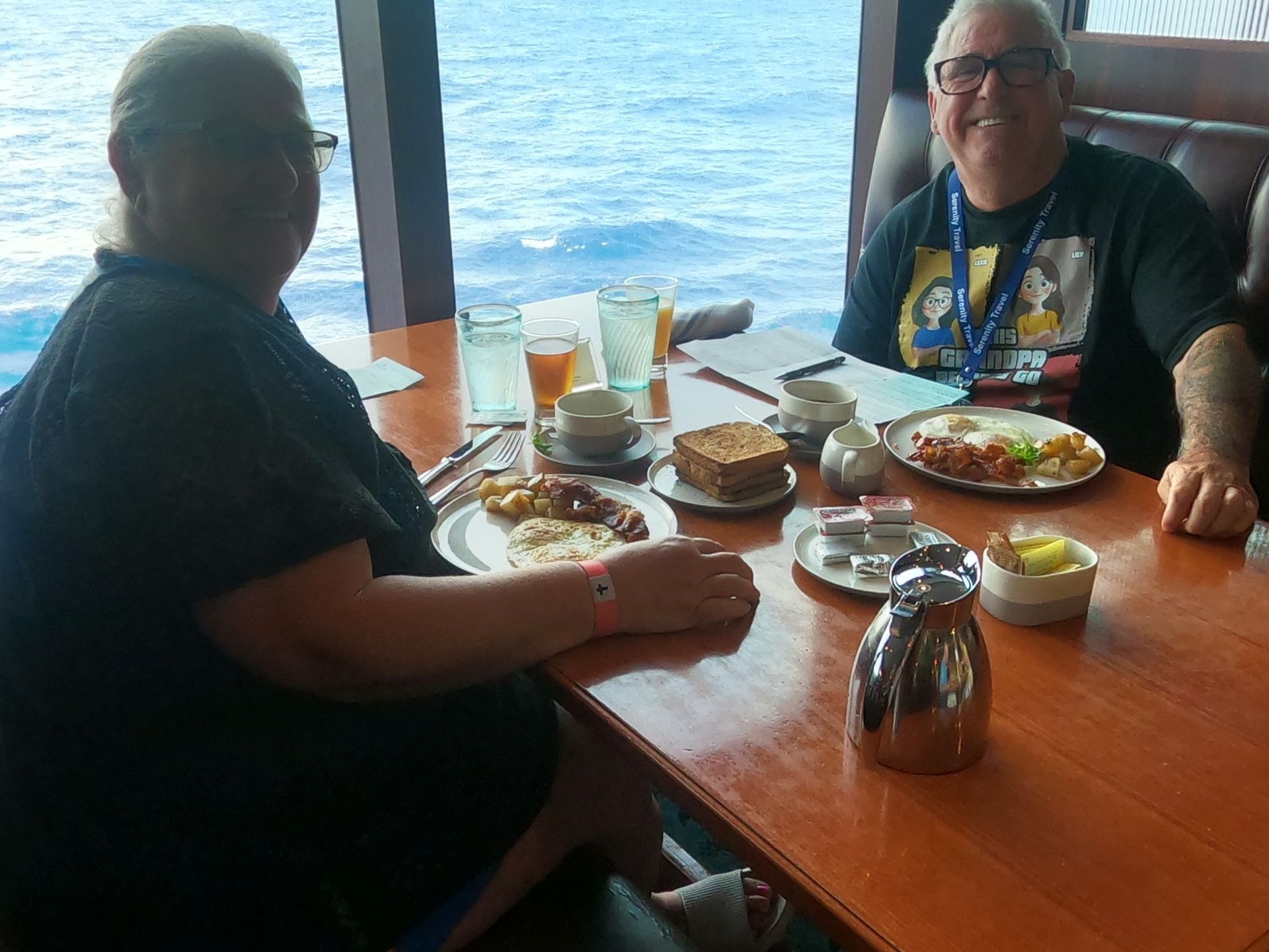 Two people enjoying breakfast by a window with ocean view. Food and drinks on the table.