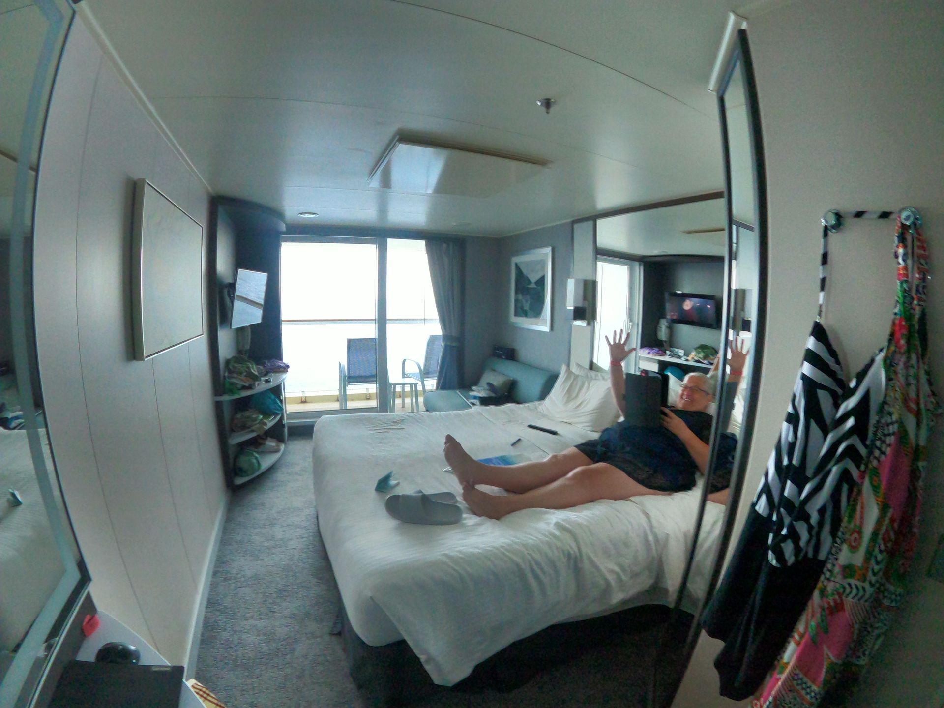 Person in a cruise ship cabin raises arms on the bed. Ocean view from the balcony.
