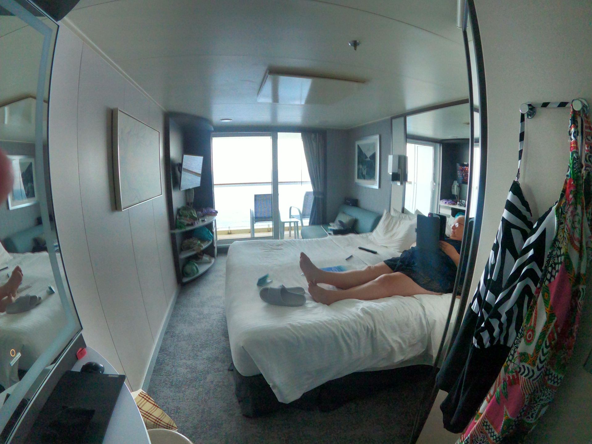 A person relaxing on a bed in a cruise ship cabin, looking at a tablet. Ocean view.