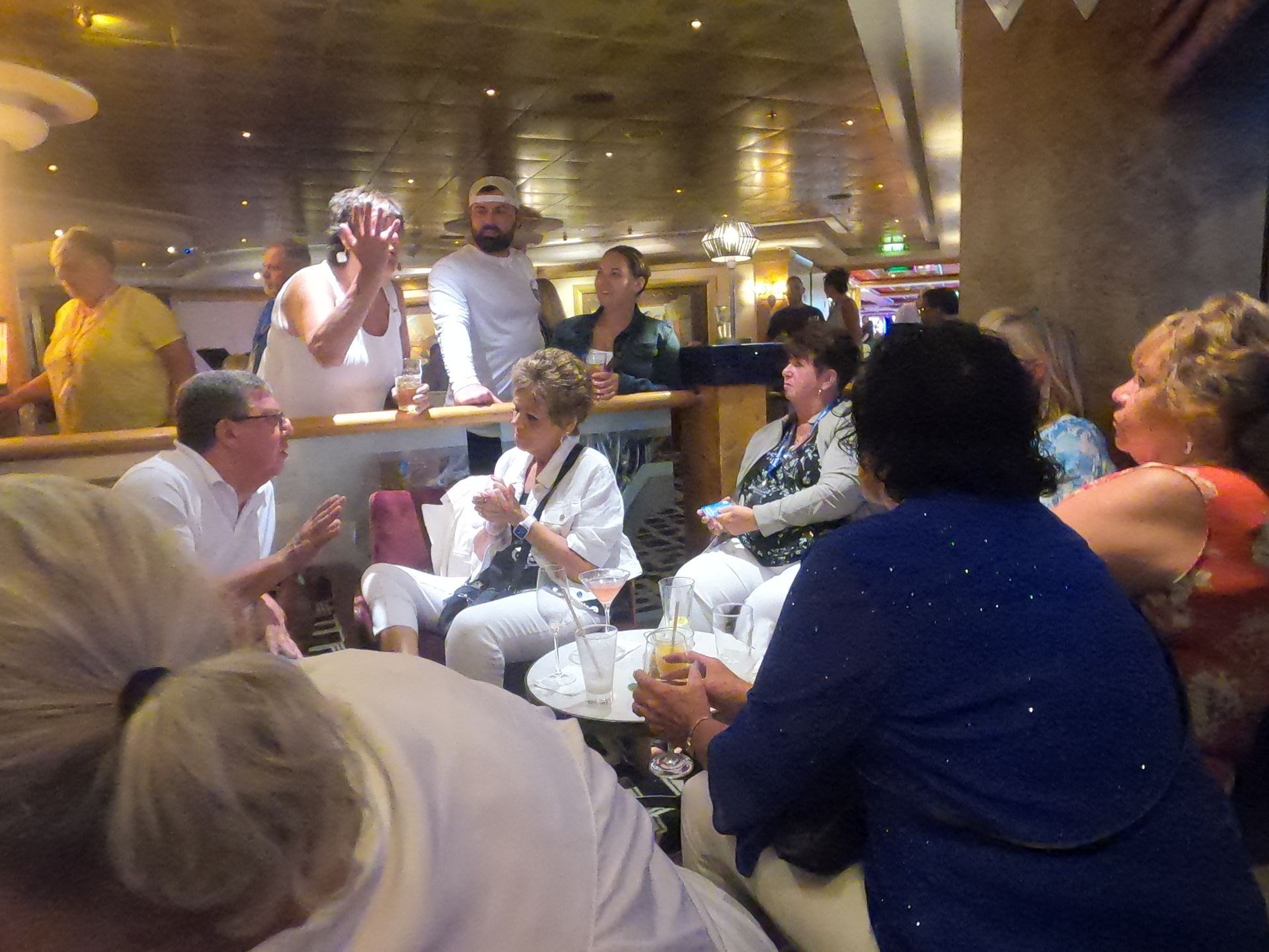 People in a bar socializing, some seated, some standing. Low lighting, neutral tones.