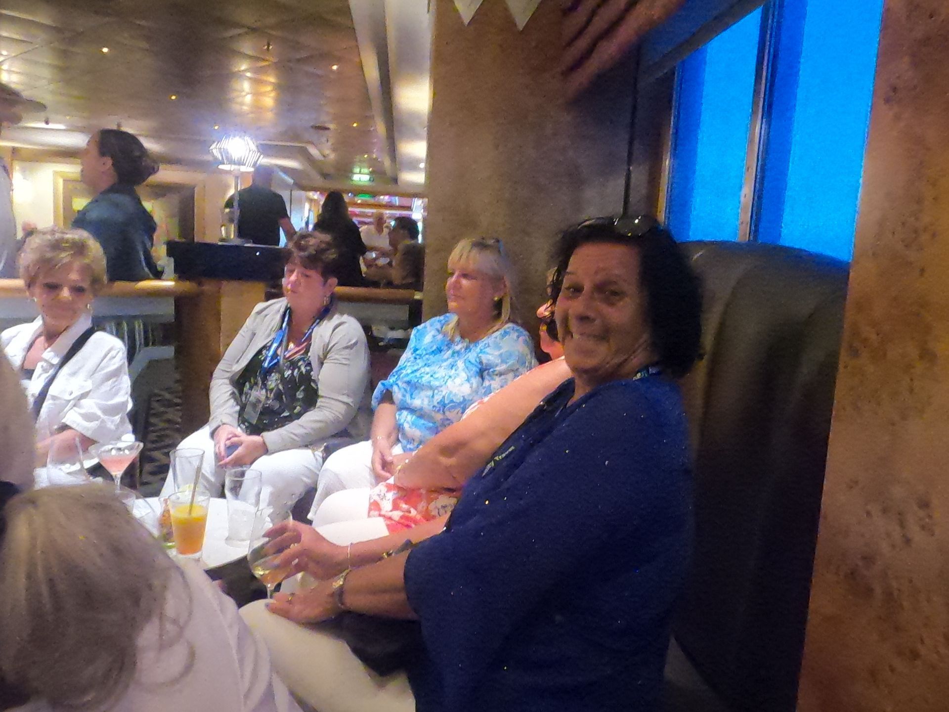 Group of women socializing in a lounge; some seated, smiling. Bright blue and orange tones.