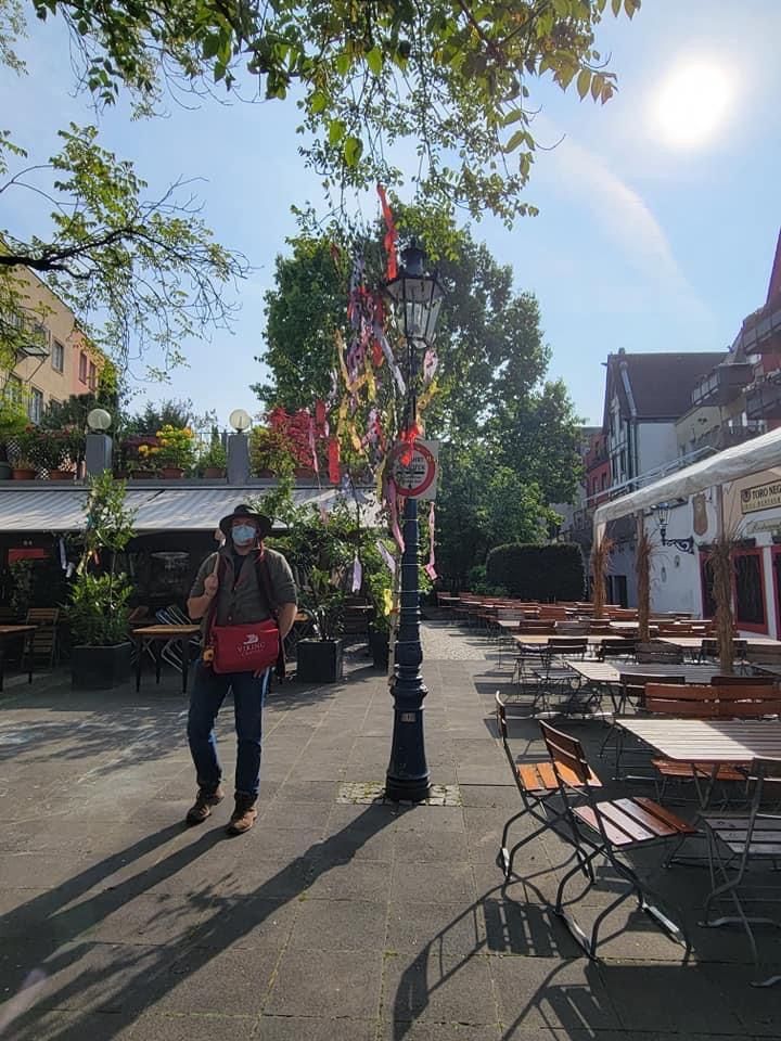 Man with a face mask walks past a lamp post decorated with ribbons at an outdoor dining area.