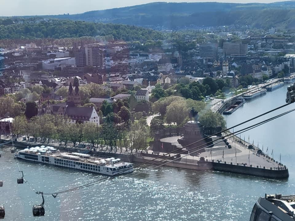 An aerial view of Koblenz, Germany, with buildings, a river, boats, and a cable car.