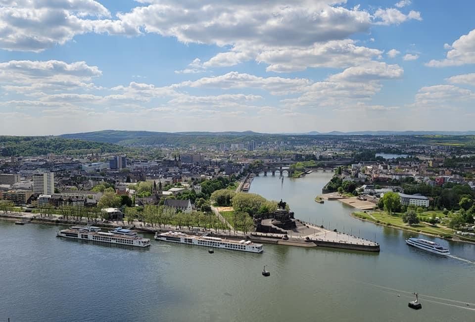 Cityscape with river, boats, and bridges under a partly cloudy blue sky.