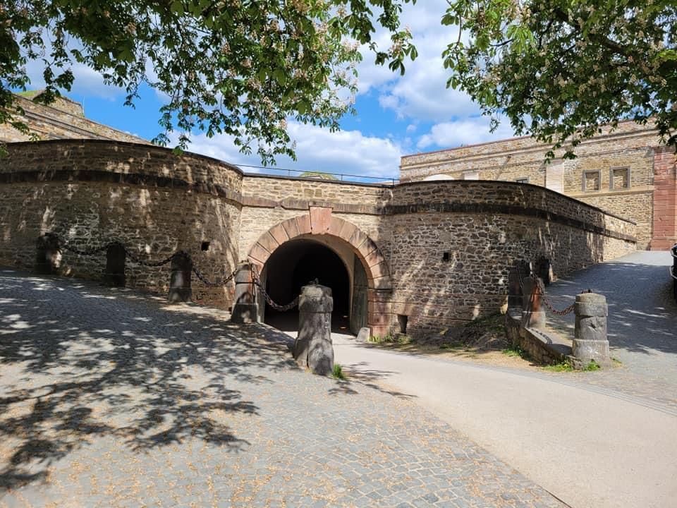 Stone castle entrance with arched tunnel, blue sky, and trees overhead.