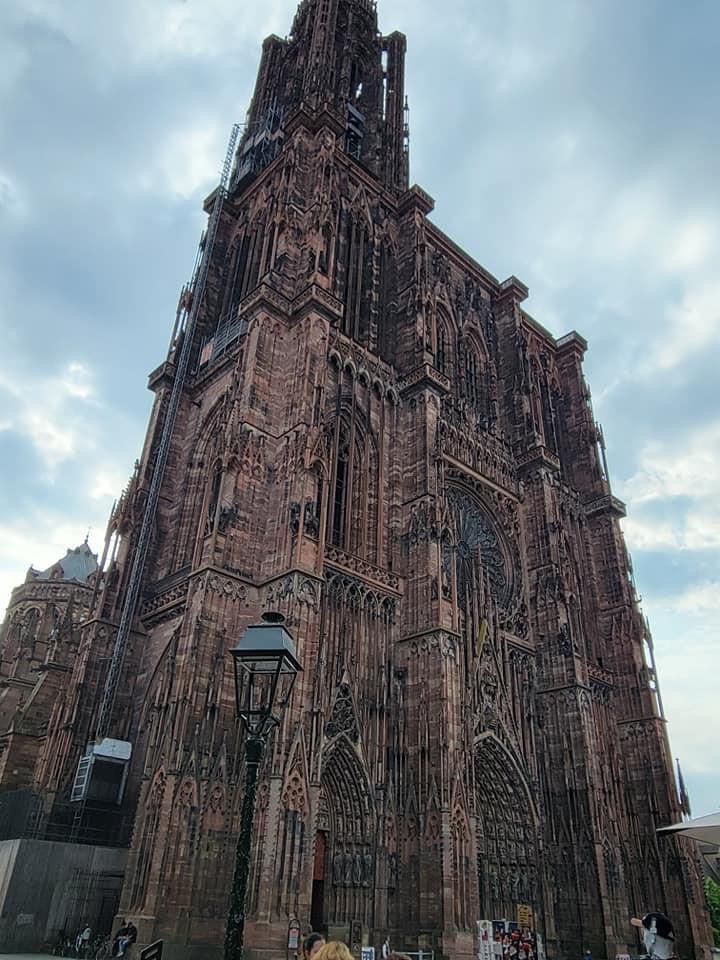 Gothic cathedral in Strasbourg, France, with intricate facade, brown stone, and cloudy sky backdrop.