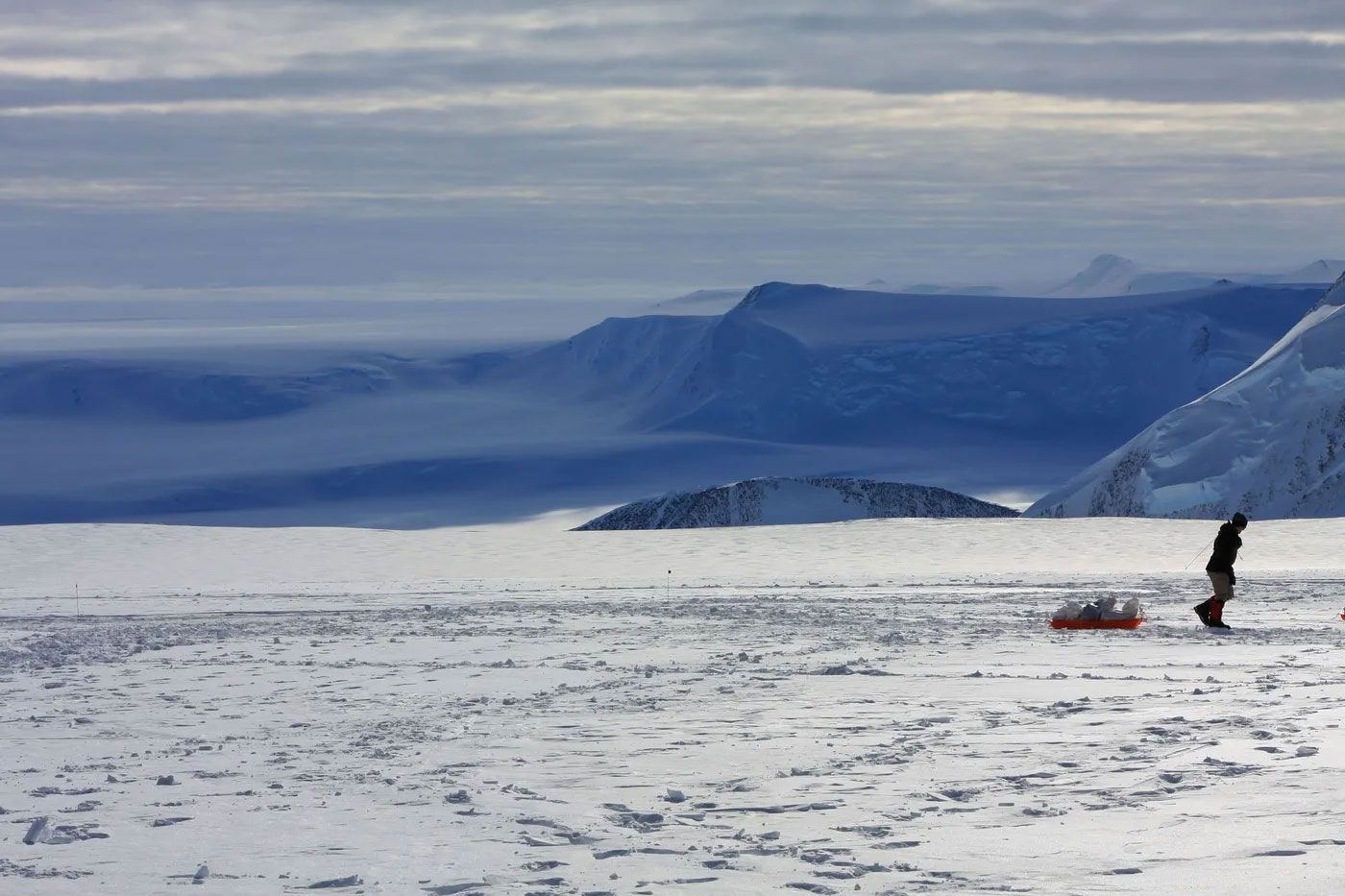 A person pulling a sled in the snow with mountains in the background