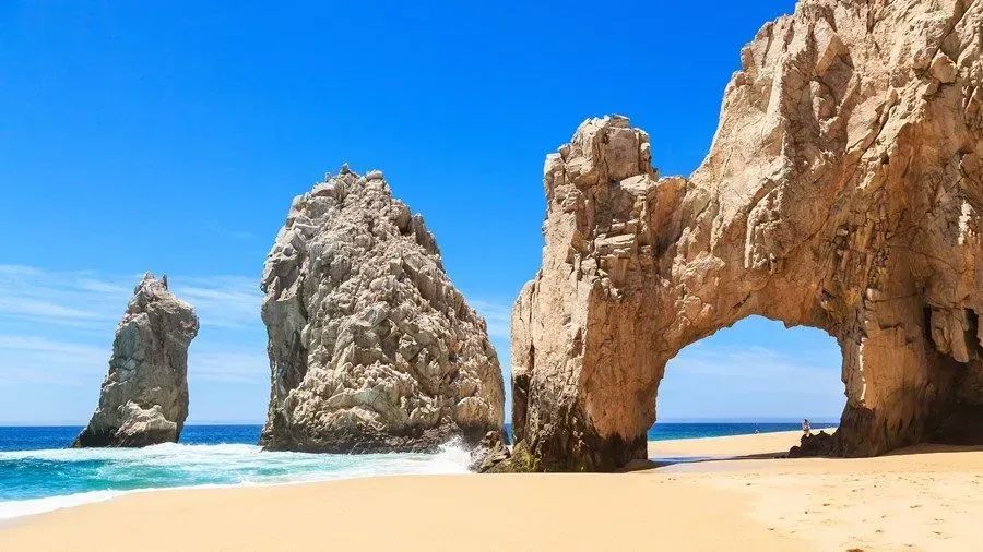 A beach with a large rock formation in the middle of it.