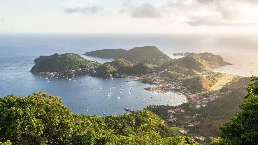 An aerial view of a small island in the middle of the ocean surrounded by mountains.