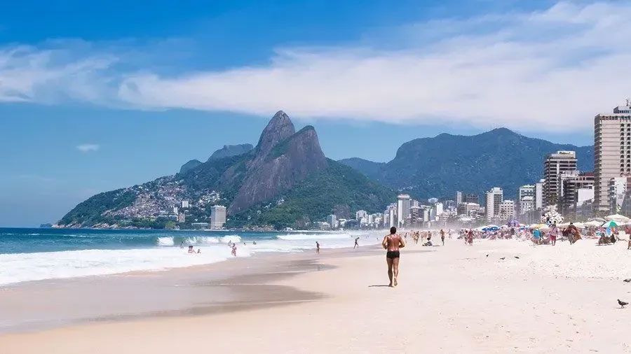 A man is running on a beach with mountains in the background.