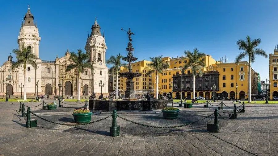 A city square with a fountain in the middle of it and a large building in the background.