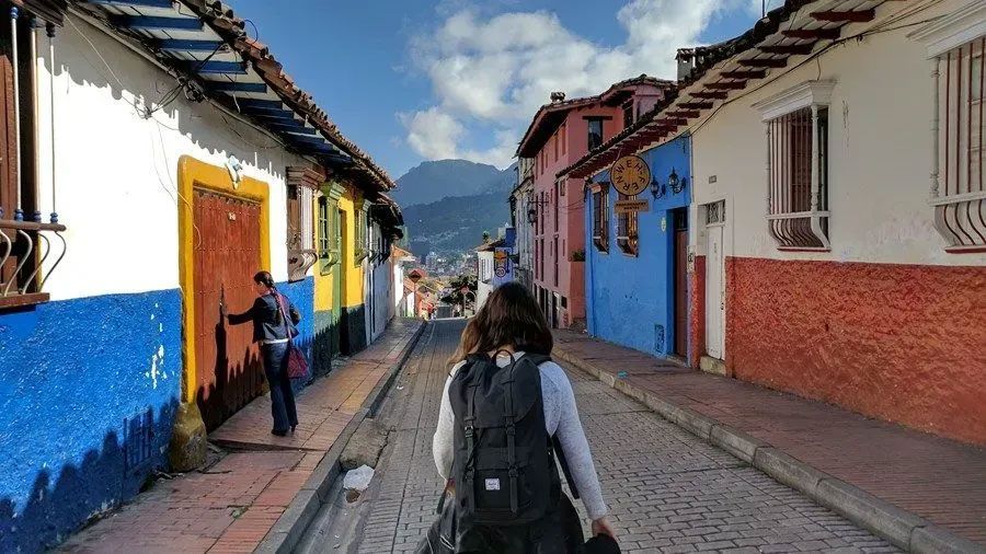 A woman with a backpack is walking down a cobblestone street.