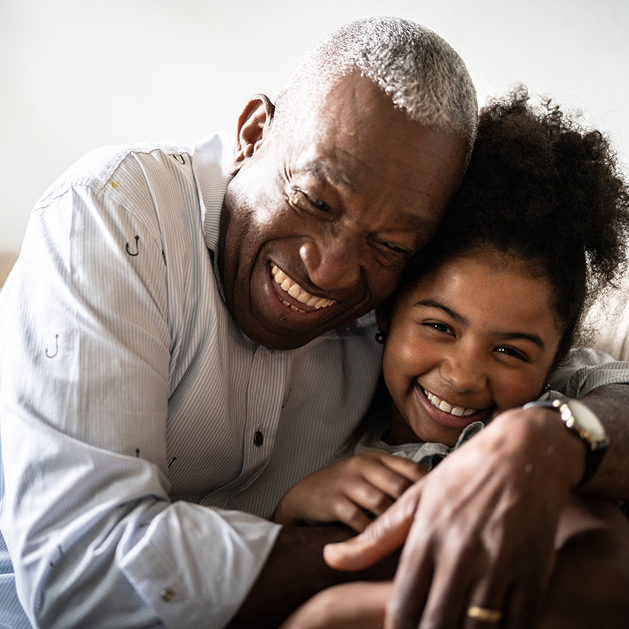 Smiling person hugs a smiling child indoors; both are happy.
