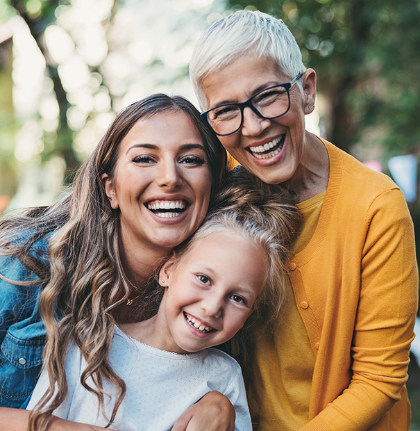 Three smiling women, embracing outdoors: grandmother, mother, and daughter.