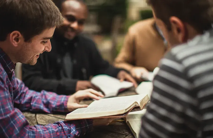 A group of young men are sitting around a table reading books.