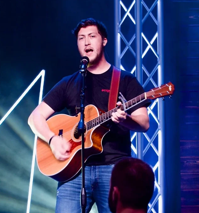 A man singing into a microphone while playing an acoustic guitar