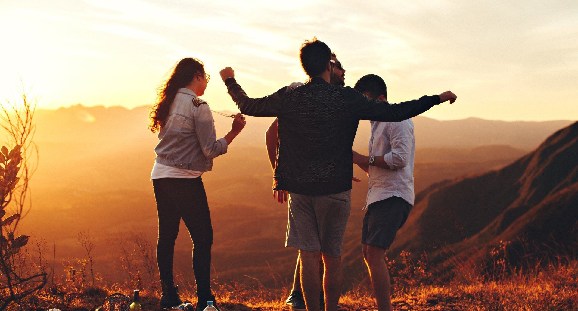 A group of people are standing on top of a mountain at sunset.