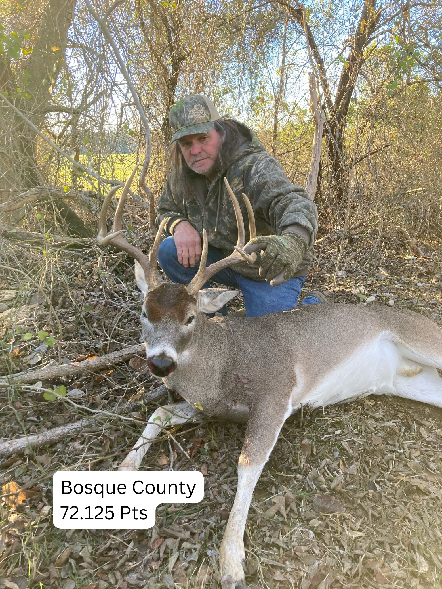 Man in camo kneels beside a buck with large antlers, Bosque County, 72.125 points.