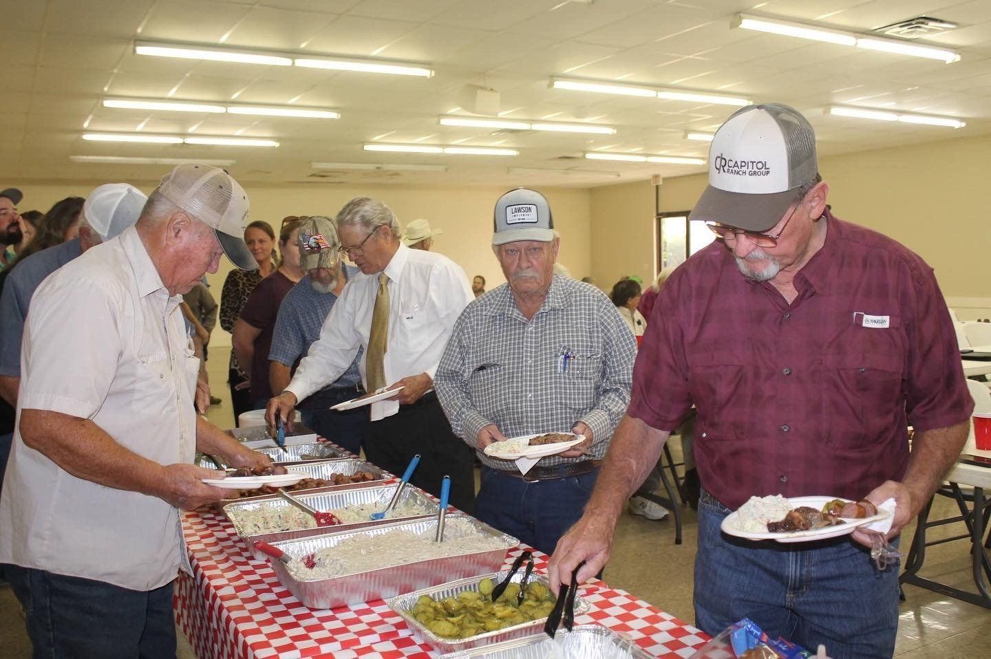 A group of men are standing around a table eating food.