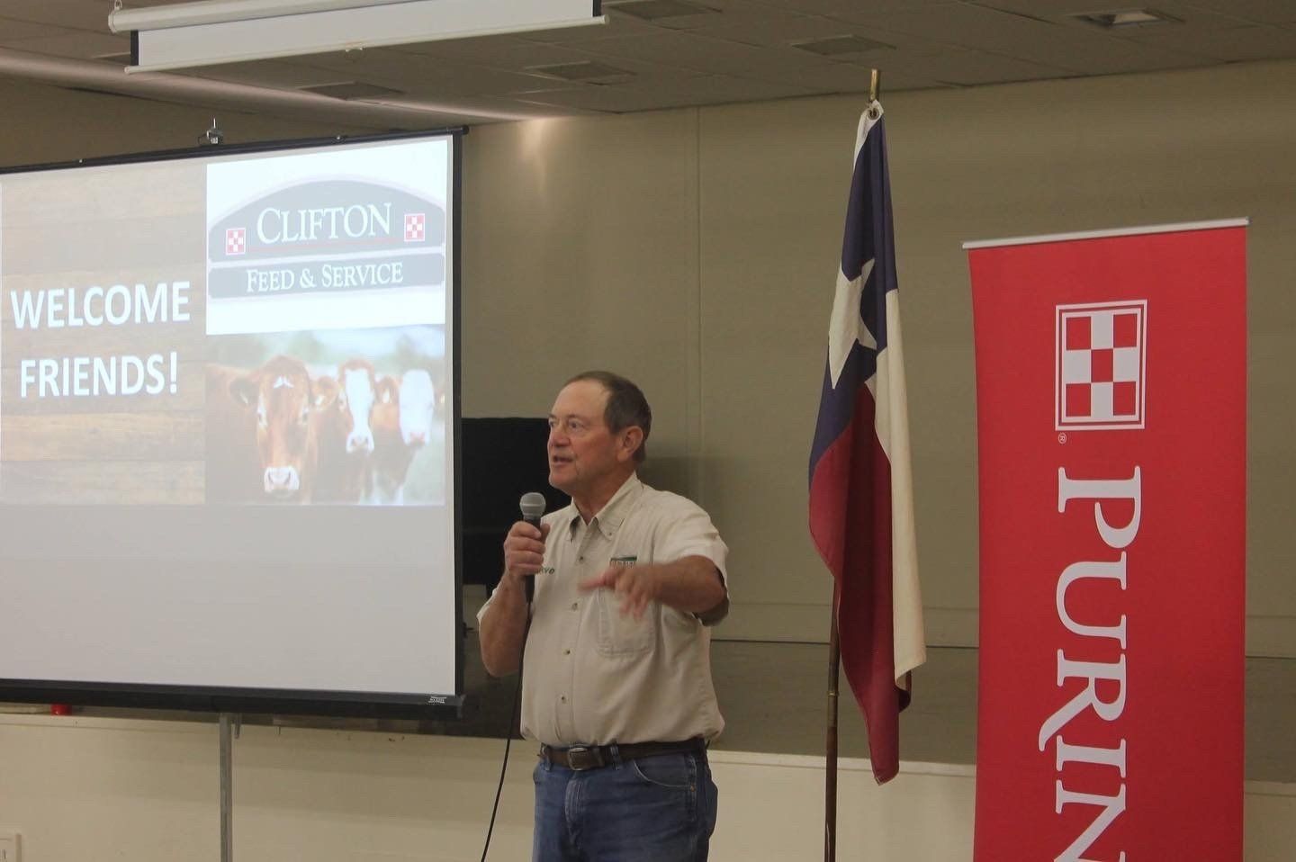 A man is giving a presentation in front of a purina banner