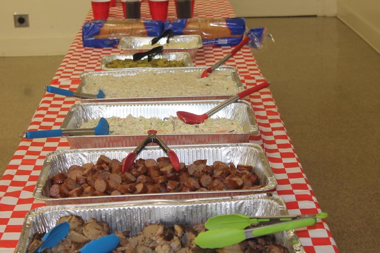 A long table with trays of food and tongs on it