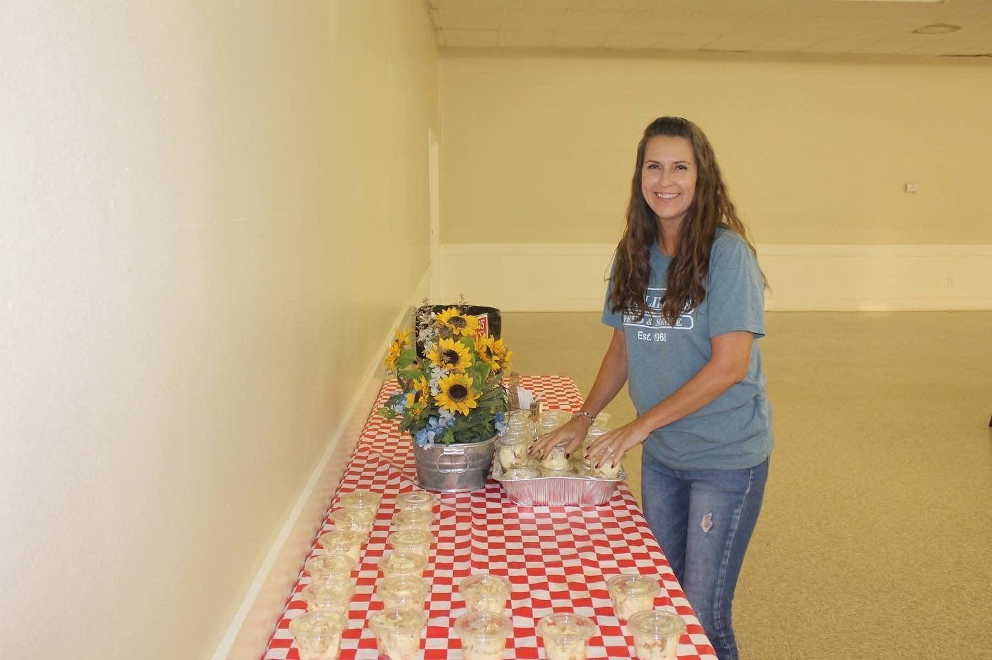 A woman in a blue shirt is standing in front of a table filled with food.